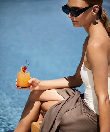 Woman in sunglasses holding fruit cocktail sitting by qualia resort pool in the Whitsundays