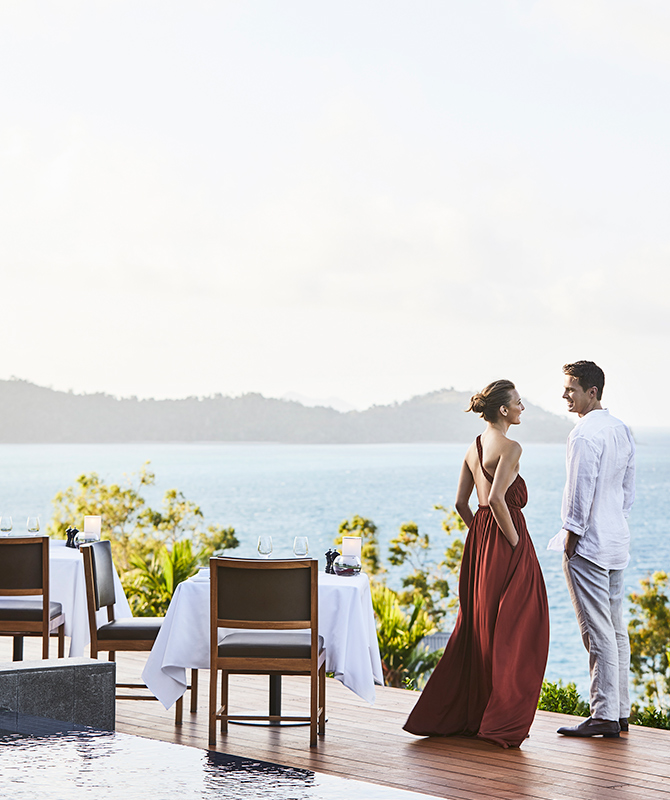 Couple standing by dinner table on Long Pavilion deck with views of the Whitsundays