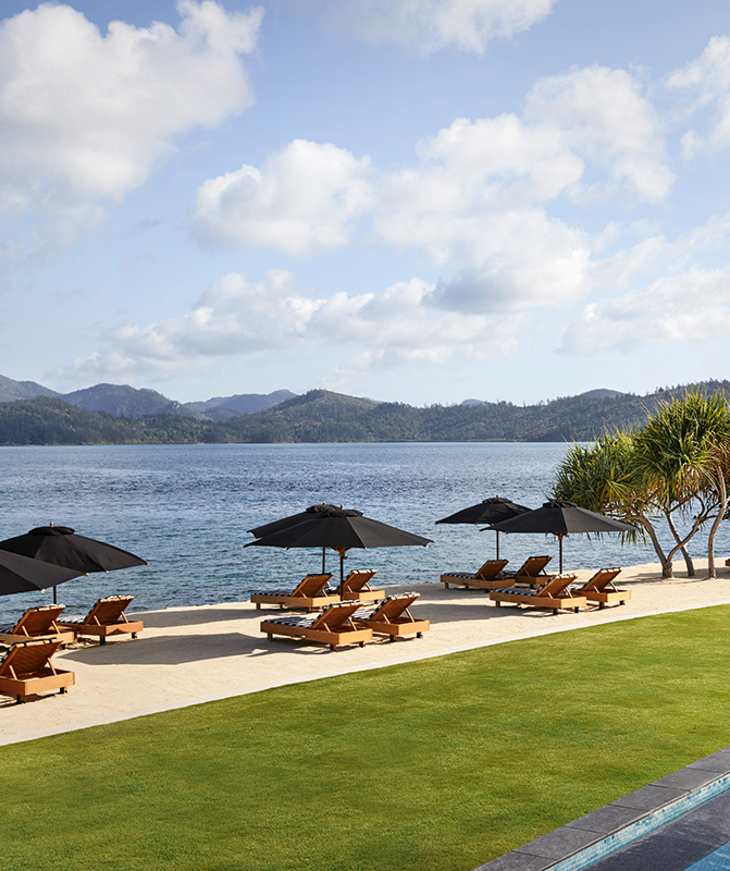 View of qualia Pebble Beach from resort pool lounges under umbrellas 
