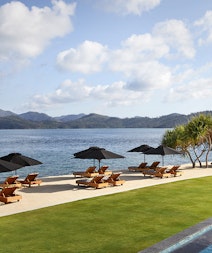 View of qualia Pebble Beach from resort pool lounges under umbrellas 