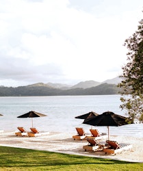 qualia Pebble Beach with sun lounges under umbrellas on the sand and views of the Whitsundays