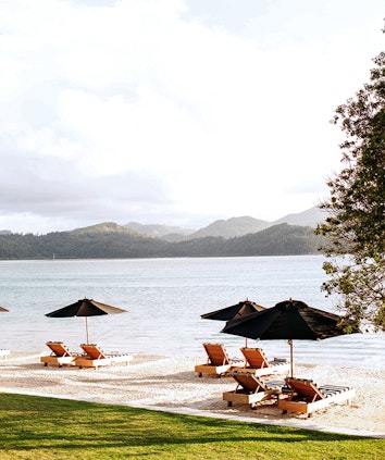 qualia Pebble Beach with sun lounges under umbrellas on the sand and views of the Whitsundays