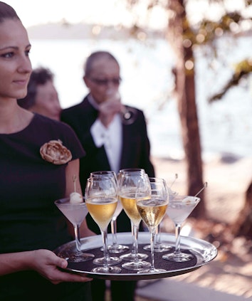 qualia female waiter carrying a tray of drinks at corporate retreat and out of focus man in the background having a drink