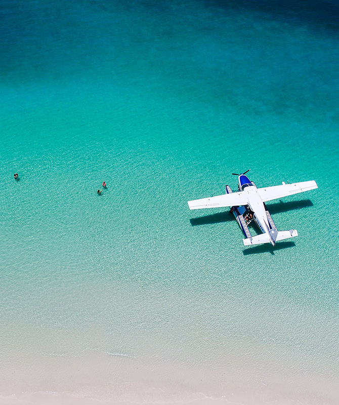Couples enjoying the water at Whitehaven Beach near sea plane as part of qualia Scenic Flight Experience