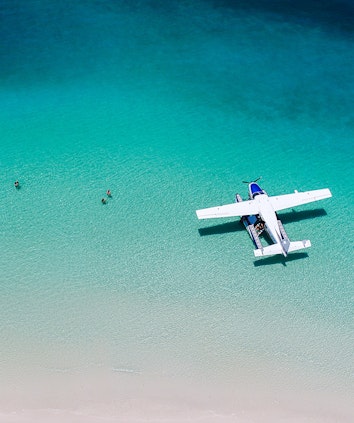 Couples enjoying the water at Whitehaven Beach near sea plane as part of qualia Scenic Flight Experience