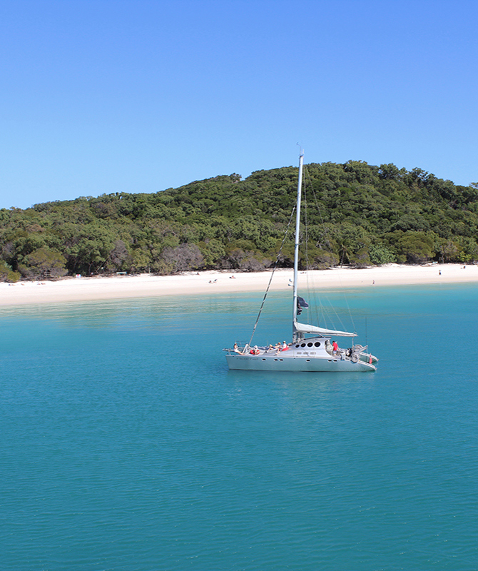 Sailors on Ricochet luxury catamaran in front of beach as part of qualia luxury experience