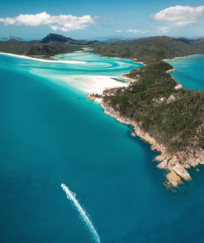 Aerial of boat leaving trail in water in front of Whitehaven Beach as part of qualia scenic flight experience