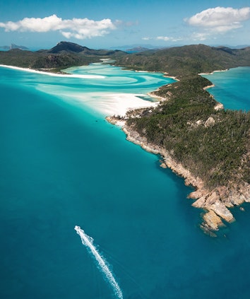 Aerial of boat leaving trail in water in front of Whitehaven Beach as part of qualia scenic flight experience