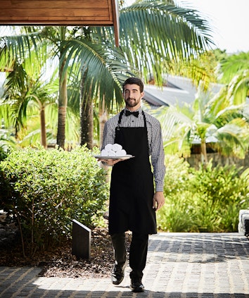 qualia resort waiter bringing tray of face towels through garden grounds