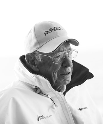 Black and white portrait of Bob Oatley wearing glasses and baseball cap with Wild Oats embroidered on it