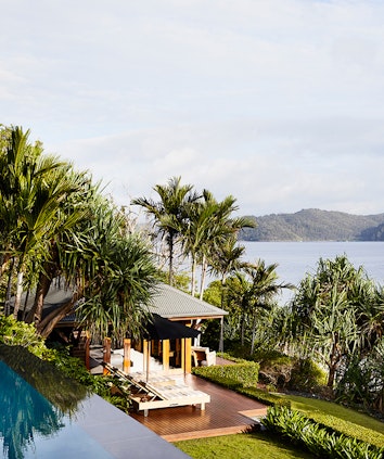 Qualia resort view of a covered Beach House deck with sun lounges and Whitsundays views surrounded by palm trees