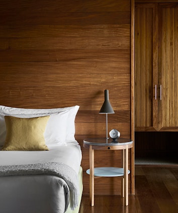 Bed with lamp and alarm clock on side table and wooden wall panelling in qualia resort Leeward Pavilion bedroom