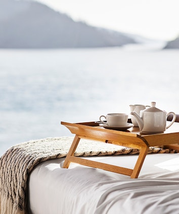 Wooden tray with teapot, cup and saucer on bed with expansive views through window of the Whitsundays