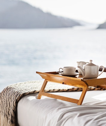 Wooden tray with teapot, cup and saucer on bed with expansive views through window of the Whitsundays