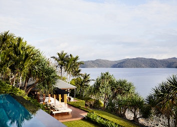 qualia resort view of a covered Beach House deck with sun lounges and Whitsundays views surrounded by palm trees