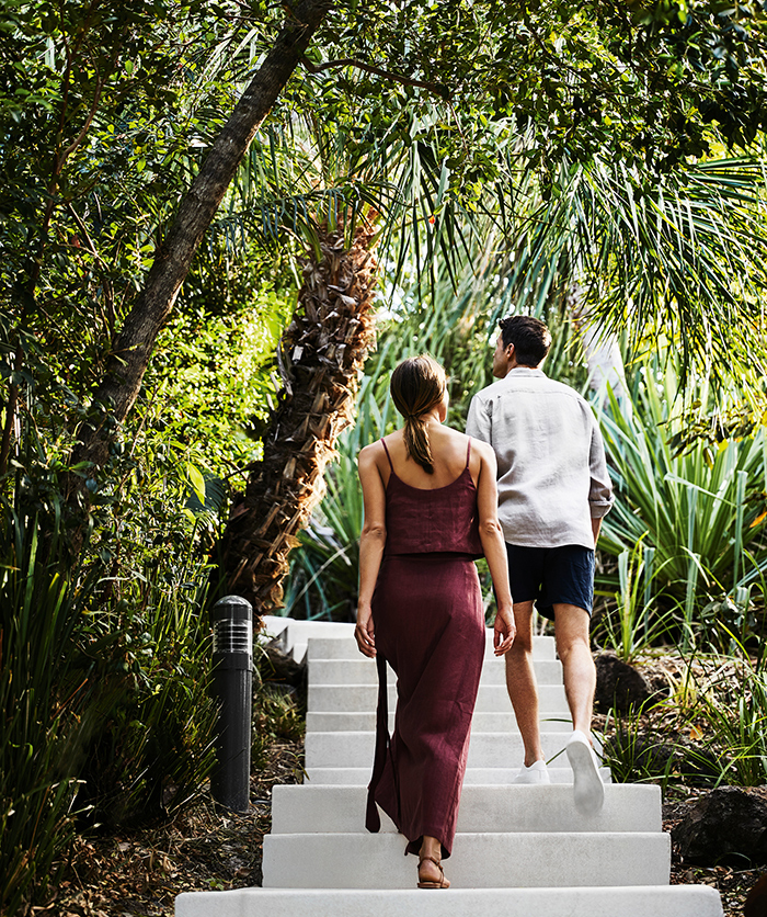 Couple walking along wooden boardwalk amongst tropical bush landscaping at qualia resort in Whitsundays