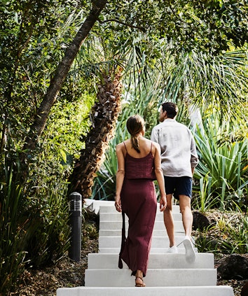 Couple walking along wooden boardwalk amongst tropical bush landscaping at qualia resort in Whitsundays