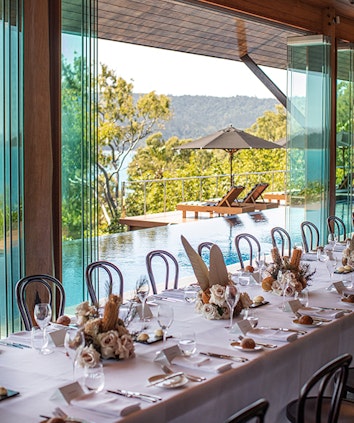 Large lunch table and chairs with flowers and outside view of infinity pool and lounges under umbrella at qualia resort 