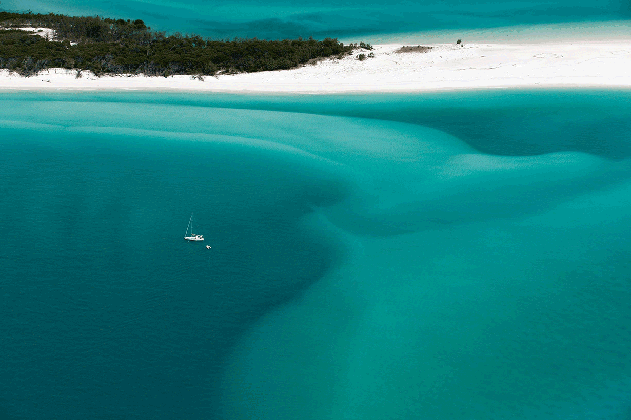 Aerial view of people enjoying waves breaking into the sand at Whitehaven Beach 