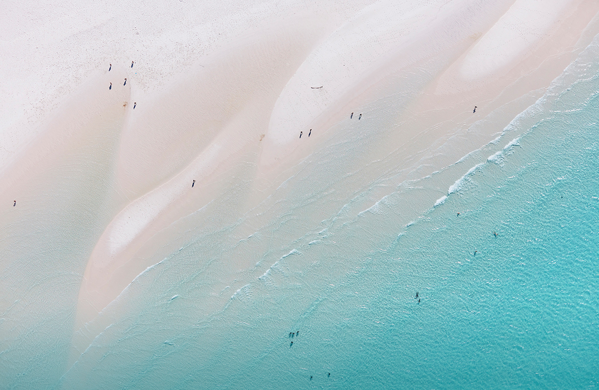 Aerial view of people enjoying waves breaking into the sand at Whitehaven Beach 