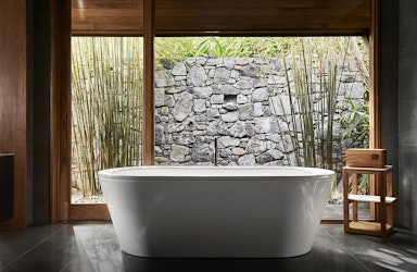 View of white bathtub and stone wall at qualia Beach House bathroom