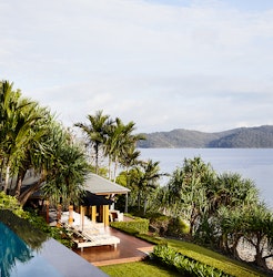 qualia resort view of covered Beach House deck with sun lounges and Whitsundays views surrounded by palm trees
