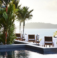 View of poolside qualia resort restaurant tables and chairs surrounded by palm trees and views of the Whitsundays 