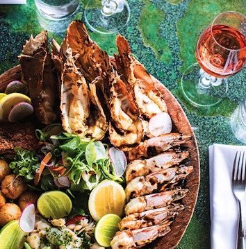 qualia resort Pebble Beach restaurant seafood platter dish with prawns, shellfish and glass of wine on green table