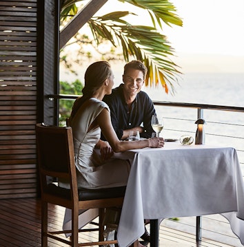Couple enjoying wine and Whitsundays views at dinner table at qualia resort restaurant Pebble Beach 