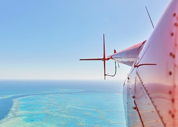 Side view of a red helicopter and its tail rotor over the Great Barrier Reef as part of qualia scenic flight experience