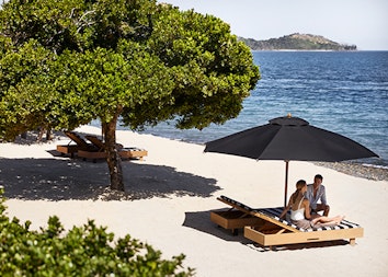 qualia resort guest couple sitting on sun lounges at Pebble Beach with Whitsundays views