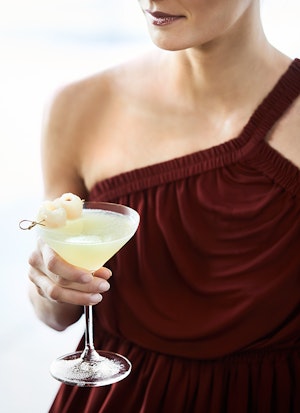 Close up of woman in maroon dress holding lychee martini cocktail at Long Pavilion bar at qualia