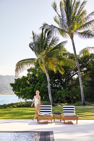 Woman in white bathing suit walking across qualia Pebble Beach pool lounges
