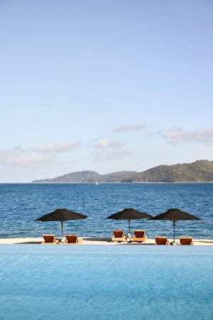 View of pool lounges under umbrellas and qualia's Pebble Beach from infinity pool 