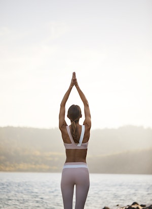  Woman with hands in prayer above head during sunrise yoga at spa qualia with view of Pebble Beach 