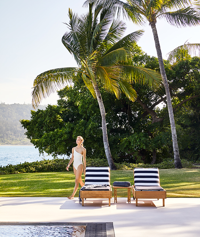 Woman in white bathing suit walking across qualia Pebble Beach pool lounges