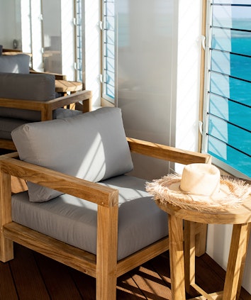 Armchair with grey pillows and raffia hat on top of side table next to a window at qualia Heart Island Lounge