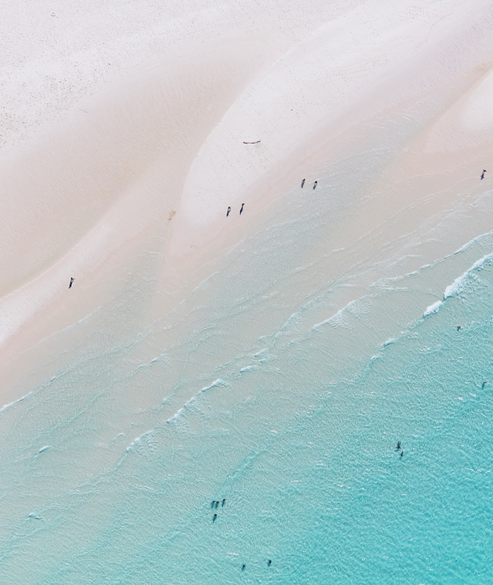 Aerial view of people enjoying waves breaking into the sand at Whitehaven Beach