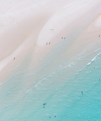 Aerial view of people enjoying waves breaking into the sand at Whitehaven Beach