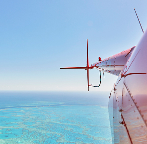 Side view of a red helicopter and its tail rotor over the Great Barrier Reef as part of qualia scenic flight experience