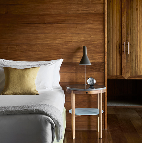 Bed with lamp and alarm clock on side table and wooden wall panelling in qualia resort Leeward Pavilion bedroom