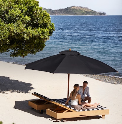 qualia Pebble Beach with man and woman sitting on striped beach lounges underneath umbrella