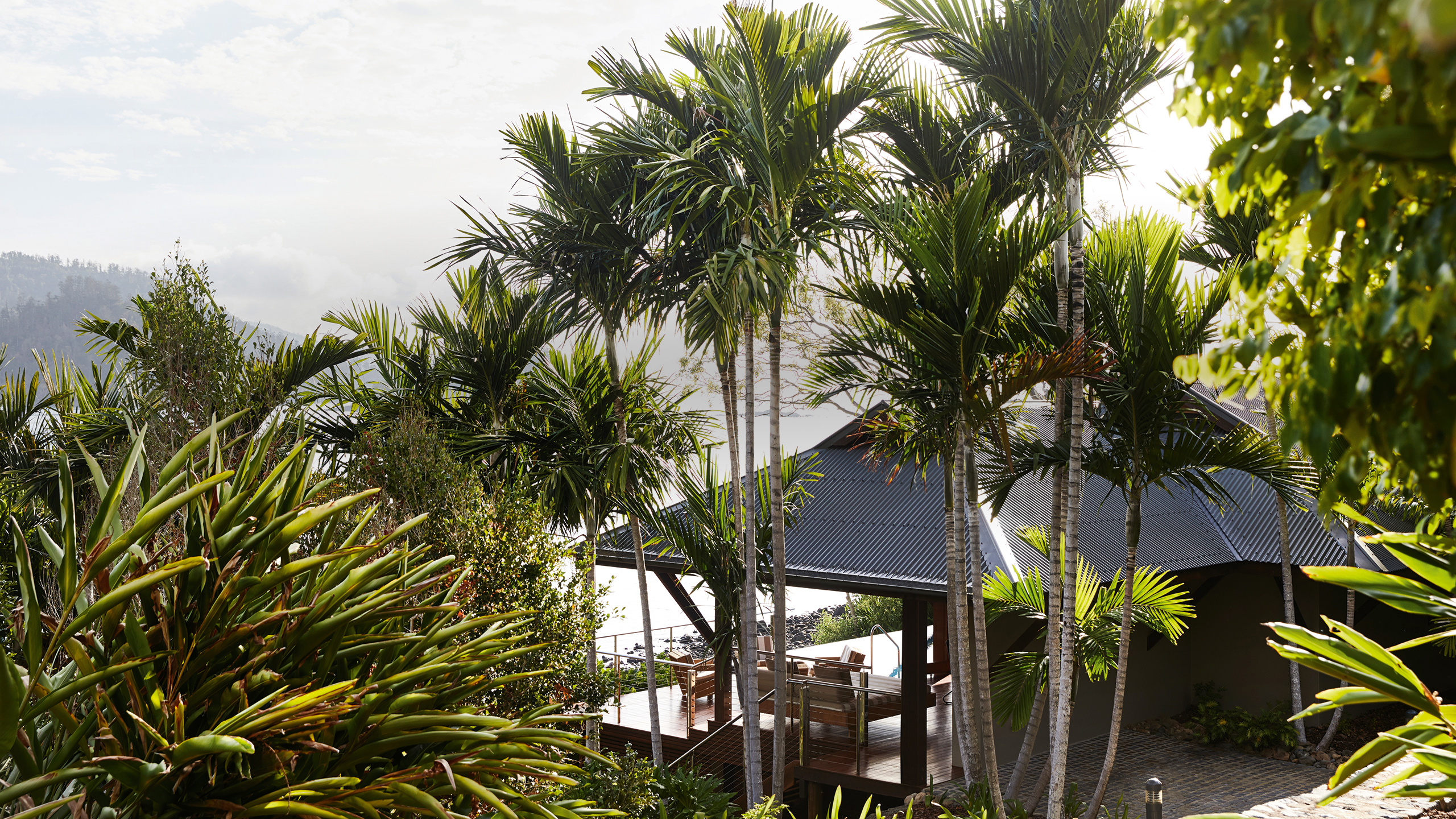 qualia resort view of a covered Beach House deck with sun lounges and Whitsundays views surrounded by palm trees