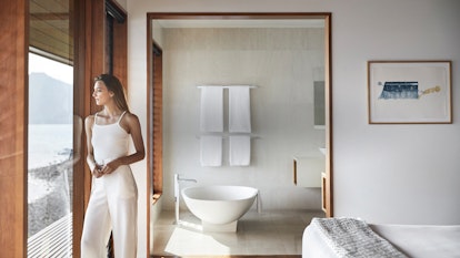 Woman standing in qualia Windward Pavilion bedroom looking at Whitsunday views with bathtub in background