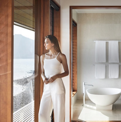 Woman standing in qualia Windward Pavilion bedroom looking at Whitsunday views with bathtub in background